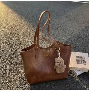 Brown vintage leather tote bag with gold lettering and cute plush dog pendant on street