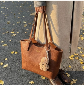Detail of vintage brown tote bag with plush bear charm on a warm autumn leaf background