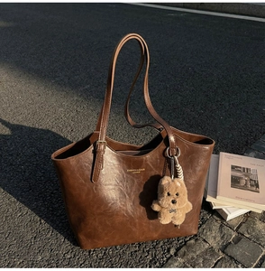 Detail of coffee brown vintage tote bag with oil wax leather texture and plush bear charm