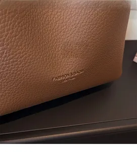 Detail of brown litchi pattern leather with embossed Fashion & Bags lettering on shoulder bag