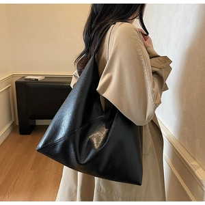 Detail of glossy black leather tote bag with subtle texture on a beige trench coat