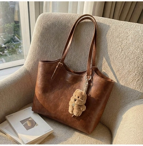 Detailed shot of a vintage brown leather tote bag with a cute plush bear charm on a sofa