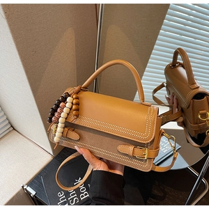Detail of vintage camel crossbody bag featuring beaded handle and strap on a book