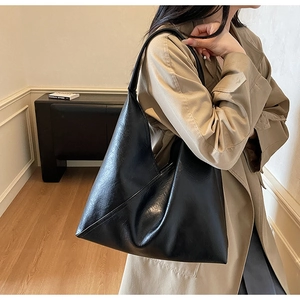 Detail of a large black faux leather tote bag showing glossy texture and shoulder strap