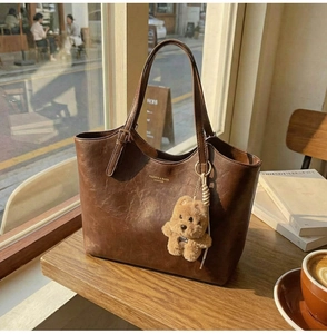 Close-up of vintage brown leather tote bag with a plush bear charm in soft sunlight