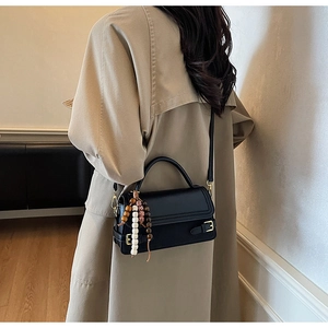 Detail of vintage matte black crossbody bag with white stitching and bead charm accessory