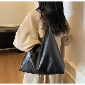 Close-up of a black oversized pebble-grain leather tote bag worn with a beige trench coat