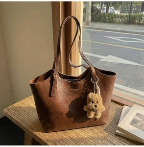 Detail of vintage brown tote bag with bear charm on a sunlit wooden bench