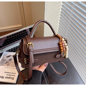 Detail of vintage matte brown leather handbag with woven flap and beaded charm