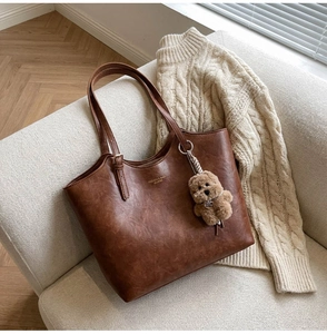 Close-up of vintage brown leather tote bag with plush dog charm on a beige sweater
