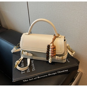 Detail of a beige matte leather handbag featuring wavy edges and a wooden beaded charm