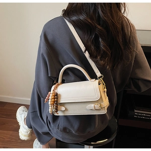 Close-up of cream square bag with vintage straps and bohemian beaded charm detail