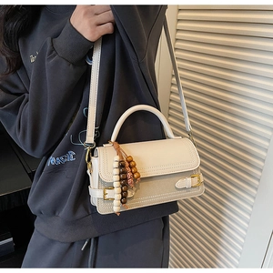 Detail of vintage cream crossbody bag with beaded tassel charm and metal buckle on strap