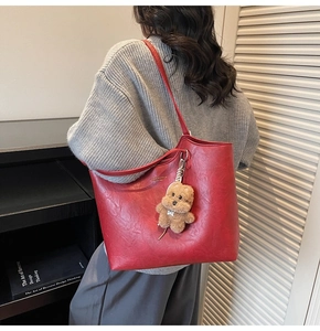Detail of red vintage leather tote bag with large capacity and brown plush bear charm