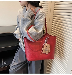 Detail of red vintage tote bag with faux leather texture and a plush bear charm accessory