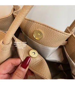 Detail of magnetic snap closure on a beige lychee grain leather underarm tote bag