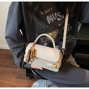 Detail of beige crossbody bag with textured patchwork and wooden bead charm accessory