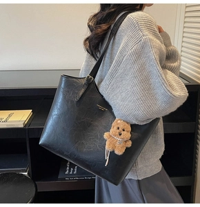 Detail of black leather tote bag with gold logo, thin straps and a cute brown bear charm