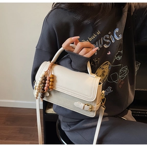 Detail of cream white crossbody bag with decorative wooden beads and fine stitching