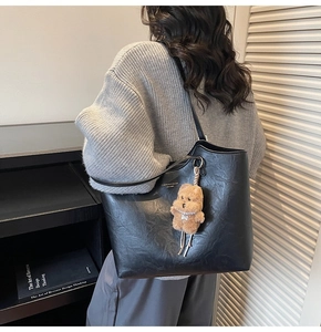 Detail of black pleated leather tote bag with a brown plush bear charm for a vintage look