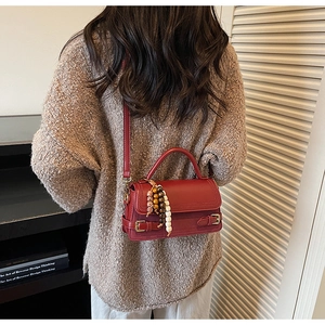 Detail of vintage red leather crossbody bag with beaded pendant on a model's outfit