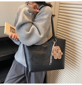 Detail of black pebbled leather tote bag with gold lettering and cute bear charm