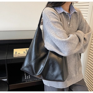 Close-up of a large black leather tote bag worn by a model in a minimalist interior