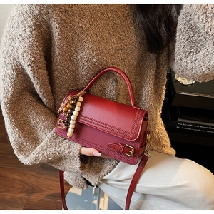 Detail of dark red vintage handbag showing leather texture, stitching and charm