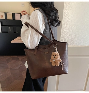 Detail of vintage brown leather tote bag with gold lettering and plush bear charm