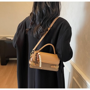 Detail view of khaki handbag with white contrast stitching and beaded tassel on model