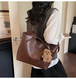 Detail of vintage brown leather tote bag featuring a plush bear charm and gold lettering
