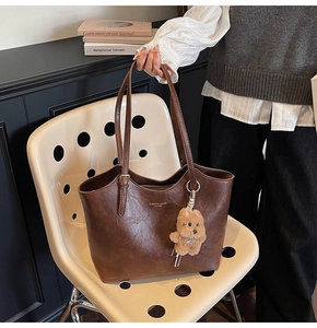 Detail of vintage brown leather tote bag with gold lettering and plush bear accessory