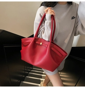 Close-up of red lychee pattern leather tote bag held by a model on dark stairs