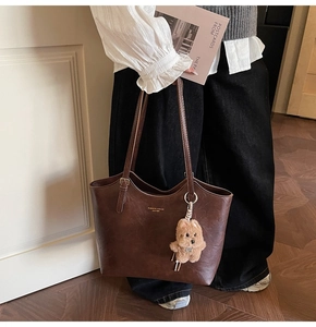 Detail of vintage brown tote bag with leather texture and plush bear charm decoration