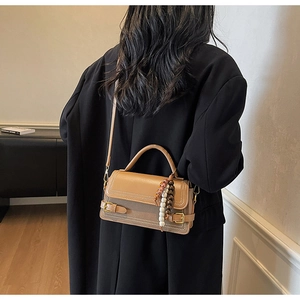 Detail of light brown matte leather crossbody bag with top handle and beaded accessory