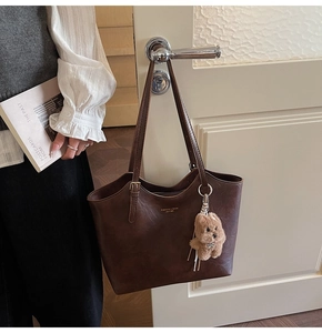 Detail of dark brown tote bag with gold lettering and cute bear plush charm hanging on door