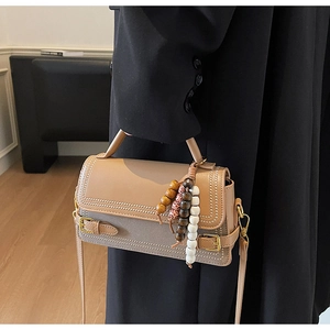 Detail of beige structured handbag with stud edges and decorative wooden bead charm