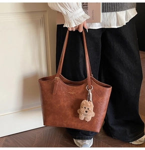 Detail of vintage brown leather tote bag with gold lettering and cute bear charm
