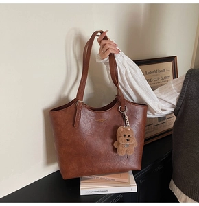 Detail of vintage brown leather tote bag with gold logo and cute plush bear charm