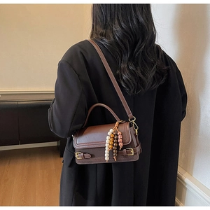 Detail of vintage brown leather crossbody bag with woven stitching and beaded pendant charm