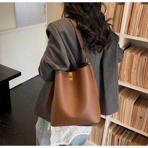 Brown leather bucket bag with gold lock shown on model in a cozy library setting