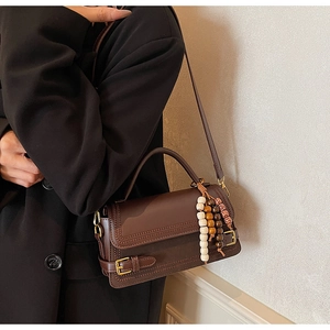 Close-up of vintage dark brown handbag with gold buckle and bohemian beaded charm detail