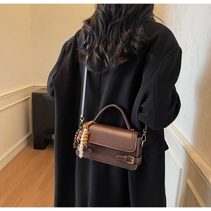 Detail of vintage coffee brown leather bag with colorful wooden beads on a coat