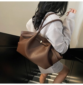 Detailed view of brown litchi leather tote bag with gold metal buckle on a shoulder