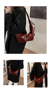 Macro detail of glossy burgundy crescent bag featuring a decorative tassel charm