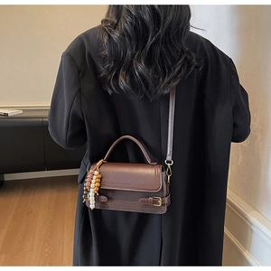 Detail of vintage dark brown handbag with stylish wooden bead tassel and crossbody strap