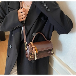 Detail of dark brown matte leather bag with adjustable strap and beaded wood tassel