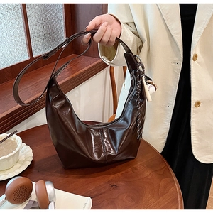 Detail of deep brown glossy tote bag with stylish baseball charm and wide strap