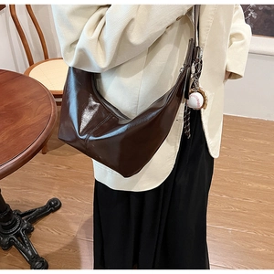 Detail of dark brown glossy crescent bag with baseball glove pendant on cream blazer