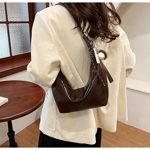 Detail of dark brown glossy hobo bag with unique baseball charm and woven strap accents